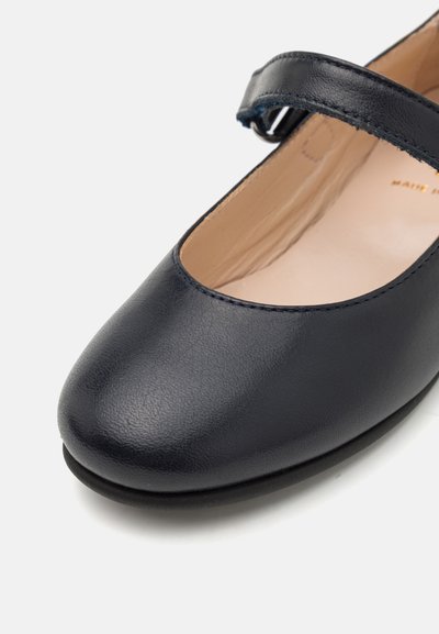 Chaussure Mary Jane en cuir bleu marine avec un bout arrondi, une sangle réglable et une semelle plate. Texture lisse avec un détail de couture minimal.