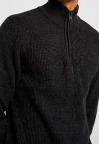 Dunkelgrauer, strukturierter Strickpullover mit hohem Kragen und einer halben Reißverschlussöffnung. Besitzt gerippte Einsätze für zusätzliche Wärme und Komfort.