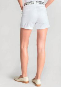 Witte spijkerbroekshorts met opgerolde zoom en een gebloemde tailleband. Gecombineerd met beige instappers. Close-up van de achterkant.