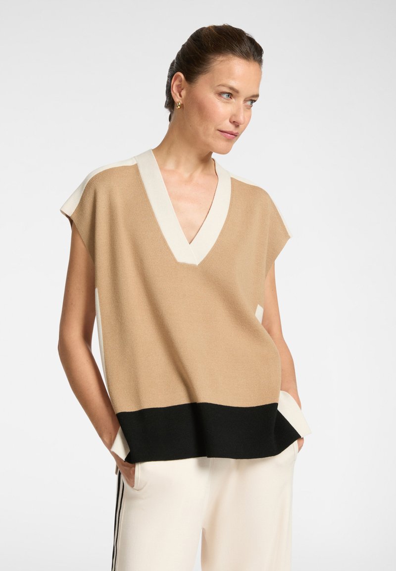 Top sin mangas de punto en color beige con escote en V, detalles en crema en los hombros y un dobladillo negro. Presenta un corte holgado y bolsillos laterales.