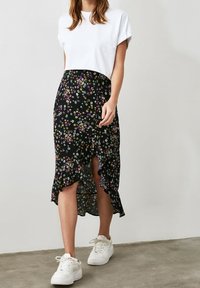 Černá midi sukně s květinovým vzorem a volánkovým lemem, zdobená malými bílými, fialovými a žlutými květy, doplněná bílým tričkem s krátkými rukávy a bílými teniskami.
