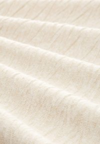 Tissu de couleur crème présentant des vagues douces et texturées avec des variations subtiles de ton, montrant des plis et une apparence lisse et confortable.