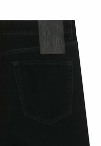 Jeans in denim nero con un'etichetta in pelle nera testurizzata con design in rilievo. Include una singola tasca posteriore con cuciture a contrasto.