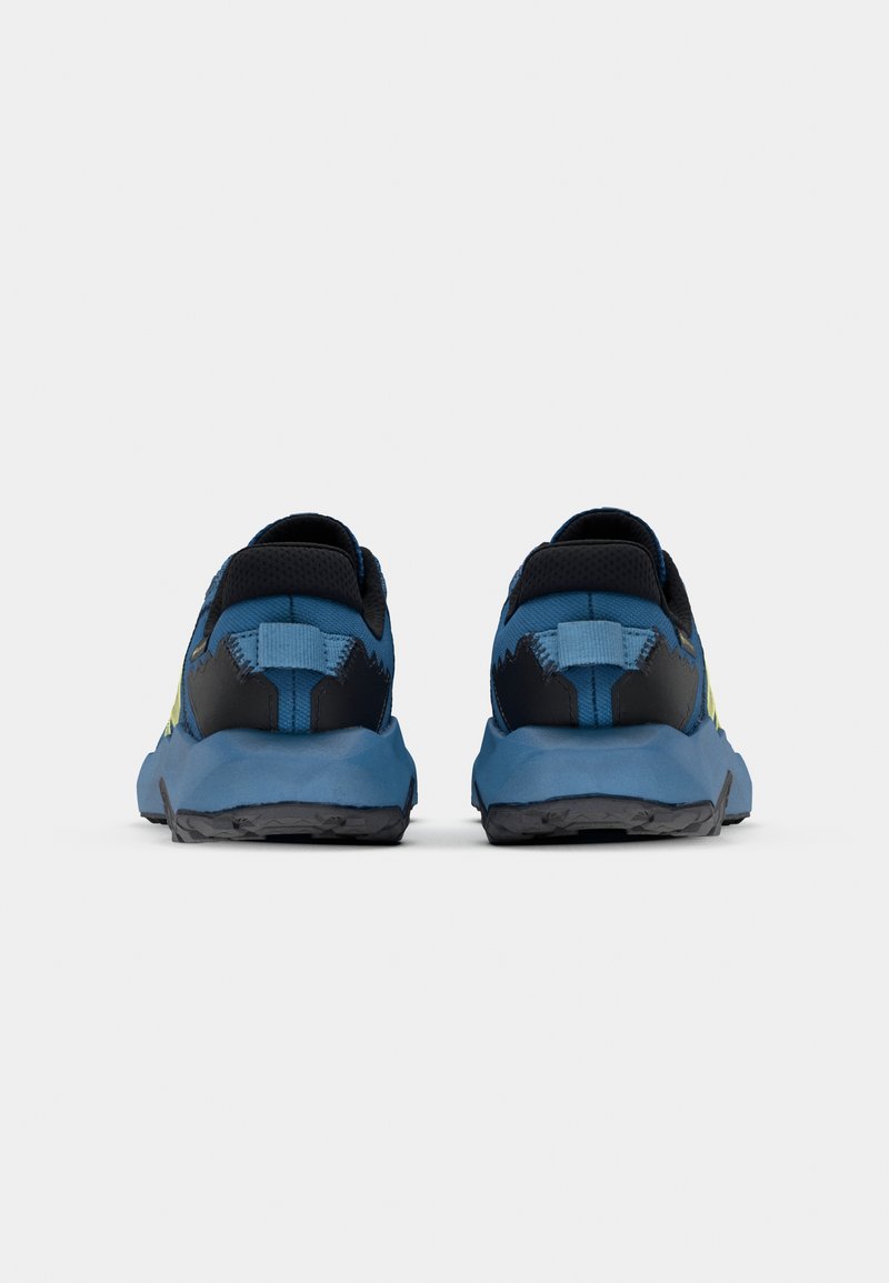 Chaussures de sport bleu et noir avec une tige texturée, présentant un accent jaune, une semelle robuste et un design de talon distinctif.