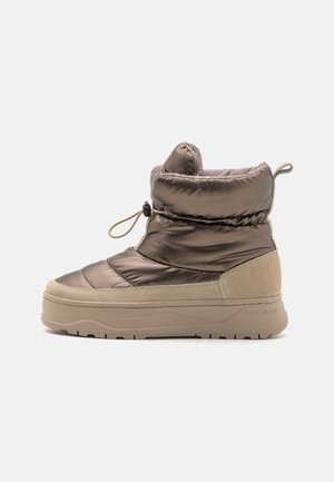 Gevoerde enkellaars met een glanzende bruine synthetische bovenkant, suède accenten, een ronde teen en een gestructureerde beige zool met een lus.