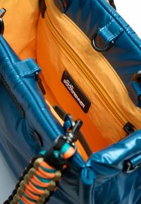 Blauwe, glanzende materiaal tas met oranje interieur; beschikt over een ritsvak, zwart logo label en kleurrijke geweven strap details.
