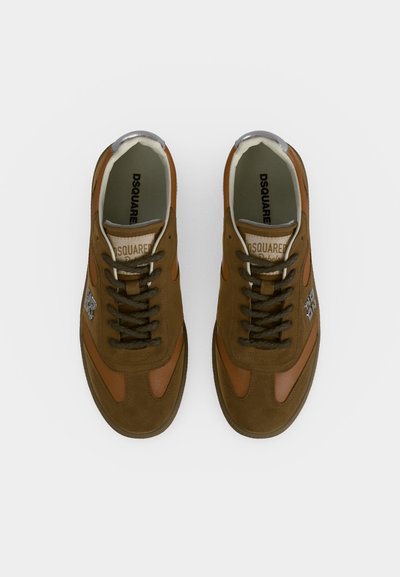 Baskets en daim marron et beige avec des lacets foncés, logo argenté sur les côtés et semelles intérieures de marque, vues de dessus sur fond blanc.
