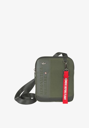 Borsa a tracolla quadrata verde oliva con tracolla nera, emblema argentato e portachiavi rosso con la scritta "REMOVE BEFORE FLIGHT".