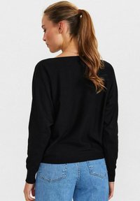 Maglione nero a maniche lunghe con una vestibilità ampia, polsini a coste e scollatura a barca, abbinato a jeans azzurri chiari. Tessuto morbido.