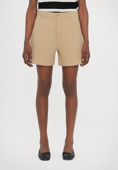 Beige bomulds shorts med flad front, opsmøgede kanter og frontlommer. Båret med sorte hæle og en sort-hvid stribet top.