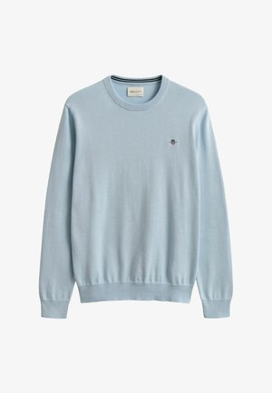 Vaaleansininen pyöreäkauluksinen neulepaita pitkillä hihoilla ja pienellä kirjotulla logolla vasemmassa rinnassa.