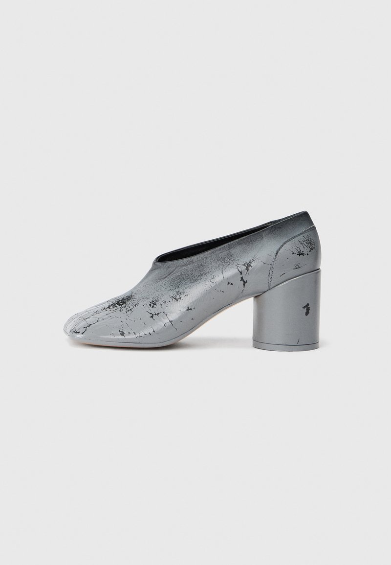 Chaussure basse en cuir grise à talon bas avec un design éclaboussé de peinture noire, présentée en profil latéral sur fond blanc.