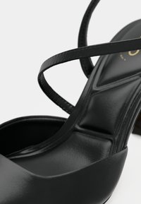 Sandale à talon haut noire en cuir lisse, dotée de brides croisées et d'une semelle intérieure profilée pour un meilleur soutien.