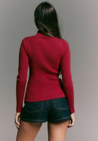Punane ribadega kudumisse sweater kõrge kaelusega, pikkae varrukatega ja istuva lõikega, sobib tumedate teksashortsidega. Sujuv tekstuur ja hästi istuv. 