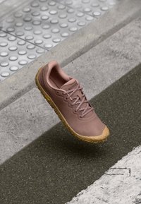 Chaussure de sport rose clair avec un dessus texturé et une semelle en caoutchouc marron clair. Elle dispose de lacets plats et d'un design lisse pour une utilisation active.