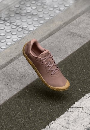 Chaussure de sport rose clair avec un dessus texturé et une semelle en caoutchouc marron clair. Elle dispose de lacets plats et d'un design lisse pour une utilisation active.