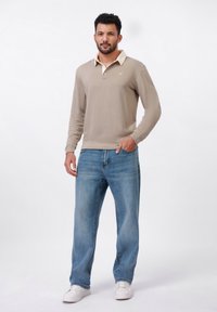 Beige long-sleeve polo with a cream collar, featuring a small yellow logo; paired with light blue straight-leg jeans and white sneakers.