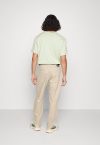 Camiseta de manga corta verde claro, pantalones beige y zapatillas. La camiseta tiene un corte relajado; los pantalones cuentan con bolsillos traseros.