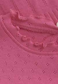 Rosa strikket bluse med volanghals, hullemønster og teksturert overflate. Sirkulær knappdetalj ved halsen.