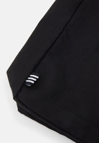 Roh černého textilního předmětu s malou černobílou pruhovanou značkou připevněnou k švu na bílém pozadí.