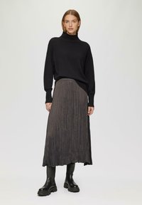 Un pull noir à col roulé associé à une longue jupe plissée gris foncé et des bottines noires, mettant en valeur la texture et le design en couches.