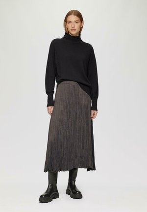 Schwarzer Rollkragenpullover kombiniert mit einem langen, plissierten, dunkelgrauen Rock und schwarzen Stiefeletten, was die Textur und das geschichtete Design betont.
