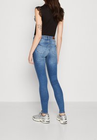 Jeans skinny de tiro alto en azul con un lavado claro, que cuentan con un diseño ajustado, bolsillos traseros y un parche de cuero marrón en la cintura.