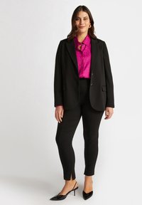 Svart blazer över en rosa leopardsmönstrad blus, i kombination med svarta slim-fit byxor och svarta slingback skor. Anmärkningsvärda slitsar vid byxornas nederkant.
