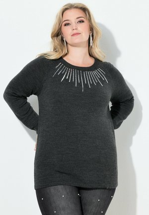 Dunkelgrauer Pullover mit langen Ärmeln, Rundhalsausschnitt und silbernen Linienmustern auf der Brust. Weicher Stoff, lässige Passform, kombiniert mit verzierten schwarzen Jeans.