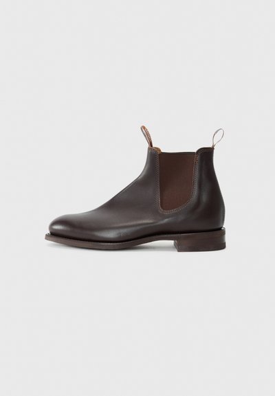 Brown leather Chelsea boot with elastic side panels, pull tab, rounded toe, and a low stacked heel. Smooth texture, minimalist design.