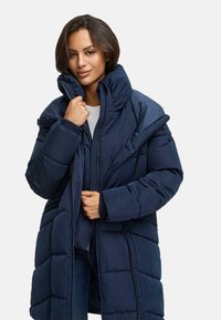 Navyblauwe gewatteerde jas met hoge kraag, gestept ontwerp, ritssluiting en ribgebreide manchetten, met een ontspannen pasvorm en gelaagde constructie.