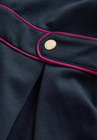 Tessuto blu navy con una trama liscia, caratterizzato da rifiniture rosa e un bottone dorato con la scritta "BAKER" incisa, che mette in risalto un dettaglio plissettato.