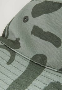 Camo-Muster-Kappe in verschiedenen Grüntönen und Grau, aus strukturiertem Stoff, mit einer runden Krone und genähtem Schirm mit Belüftungslöchern.