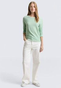 Hellgrünes, strukturiertes Langarmoberteil mit Rundhalsausschnitt, kombiniert mit cremefarbenen, weit geschnittenen Hosen und weißen Sneakers. Schlichtes und lässiges Design.