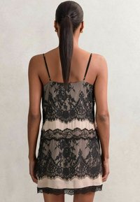 Rochie neagră din dantelă cu straturi transparente, bretele ajustabile și un strat de bază bej contrastant. Model floral delicat pe întreaga suprafață.