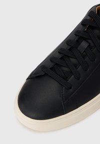 Svarte lær sneakers med avrundet tå, flate lisser og en beige gummisåle. Glatt tekstur med minimale søm detaljer.