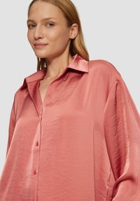 Blouse en satin rose foncé avec col pointu, fermeture par boutons, coupe loose, manches longues et texture lisse.
