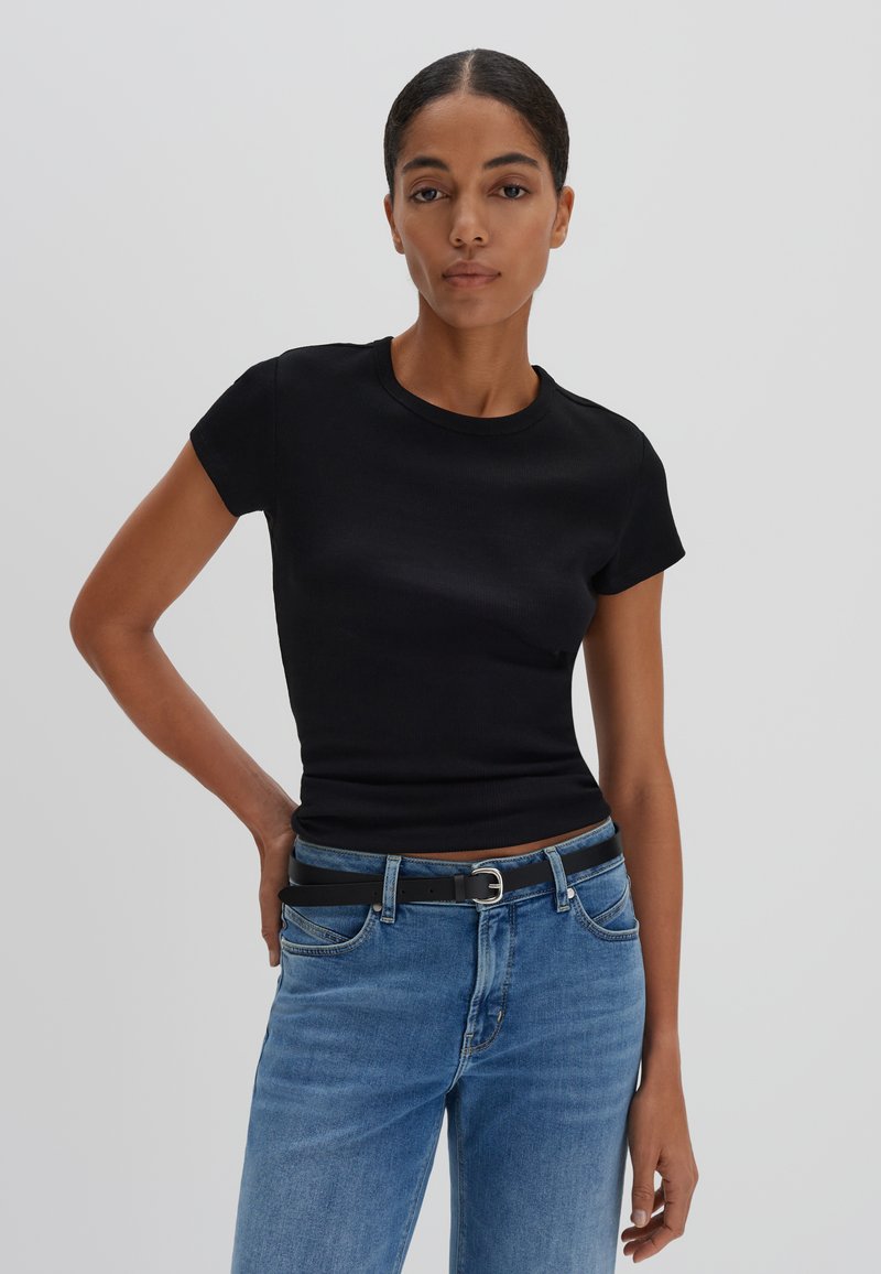 Zwarte, getailleerde t-shirt met korte mouwen van ribstof, gecombineerd met lichtblauwe denim jeans en een zwarte riem met een zilveren gesp.