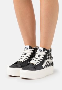 Hoge sneakers met zwart-witte patroonstof, witte veters en een dikke witte rubberen zool. Bevat het Vans-logo op de tong.