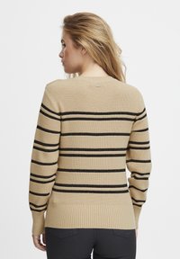 Pull en tricot beige avec des rayures horizontales noires, poignets et bas côtelés, décolleté rond, avec des fils métalliques subtils pour la texture.
