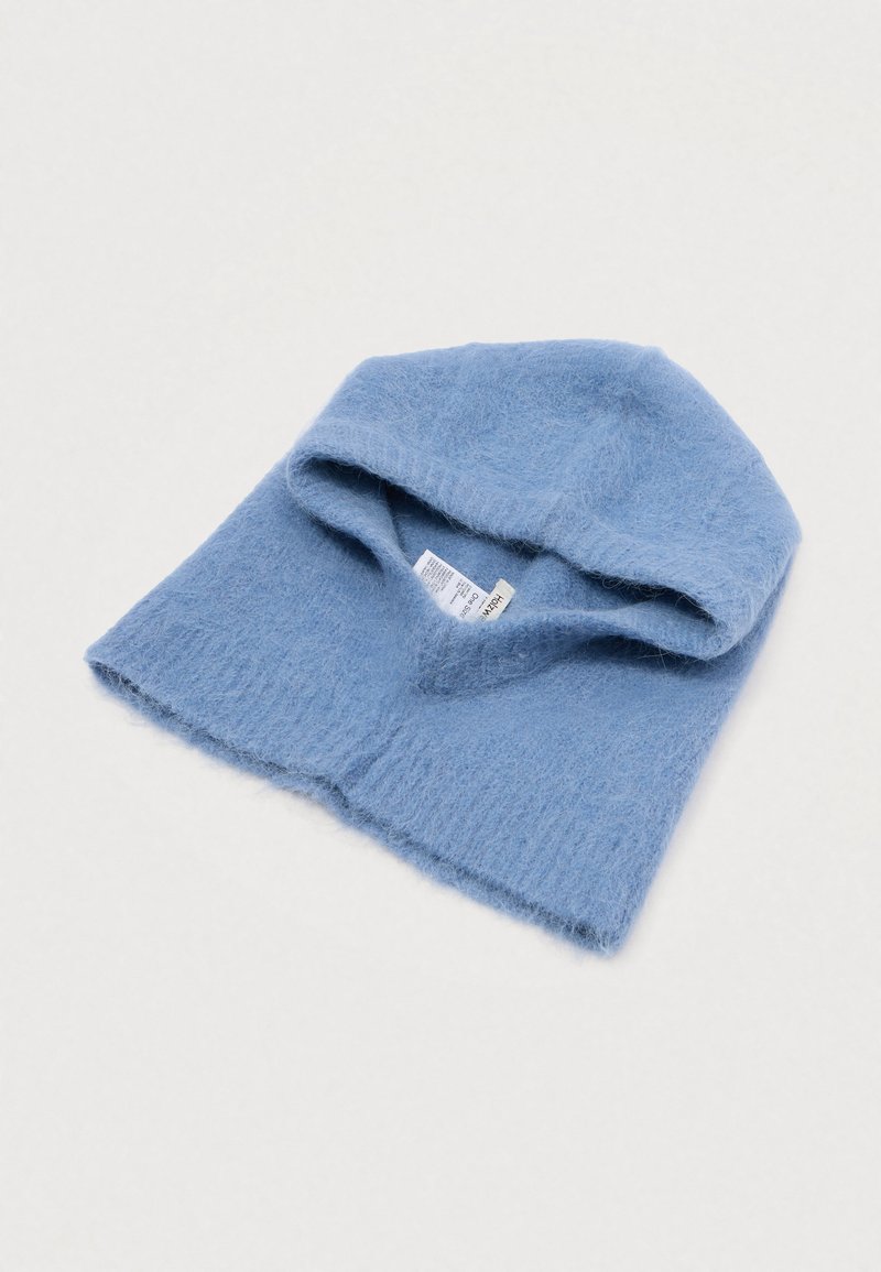 Weiche blaue Strickwolle-Balaclava mit geripptem Saum und sichtbarem Pflegeetikett innen, flach auf einer weißen Oberfläche liegend.