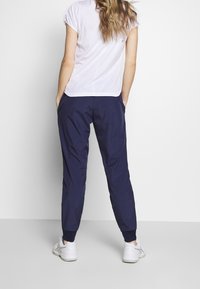 Tmavě modré sportovní kalhoty s elastickými manžetami a bočními kapsami, doplněné přiléhavým bílým krátkým tričkem s kulatým lemem.