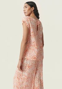 Bluse med blomsterprint i lyse fersken- og orange nuancer, med bindebånd i ryggen og korte ærmer. Letvægtigt, flydende stof.