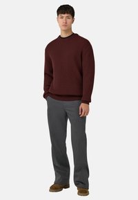 Burgundi spalvos ribota megztinys su apvalia apykakle, derinamas su pilkais kelnėmis ir rudos odos bateliais. Audinys atrodo tekstūruotas ir šiltas.