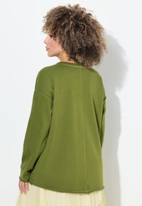 Top de manga larga color verde oliva con un corte relajado, escote redondo y detalles de costura visibles, combinado con una falda ligera en capas.