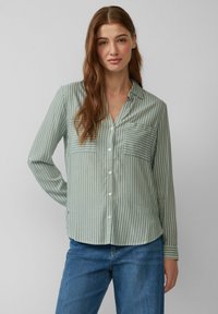 Chemise boutonnée à manches longues vert clair avec des rayures verticales blanches. Présente une poche poitrine et un ourlet inférieur arrondi. Texture de tissu douce.