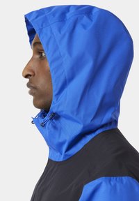 Modrá kapucňová bunda s tmavým tělem, vybavená strukturovanou kapucí, nastavitelným šňůrkovým stahováním a designem s barevnými bloky. Hladká, lehká tkanina.