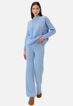 Lyseblå strikket sweater med et kabelmønster, parret med matchende brede bukser. Begge dele har en blød tekstur. Brune sko fuldender looket.