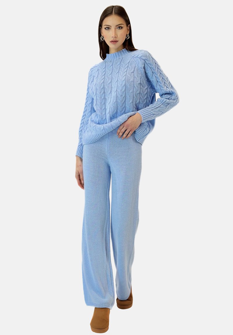 Un suéter de punto azul claro con un patrón de trenzas, combinado con pantalones de pierna ancha a juego. Ambos artículos tienen una textura suave. Footwear marrón completa el look.