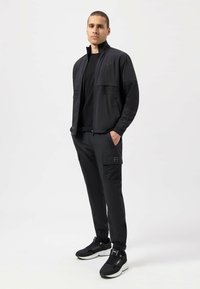 Black athletic jacket with mesh accents, paired with matching pants featuring cargo pockets. Completed with black sneakers.